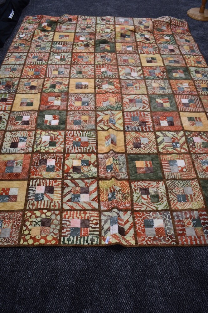 A large retro quilt made up of sections of autumnal shades of tie dyed cotton.