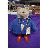 A Gabrielle Designs plush covered Padding Bear soft toy, wearing blue jacket and red wellingtons,