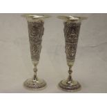 Two Indian white metal bud vases having embossed decoration depicting deities, no marks, one rim