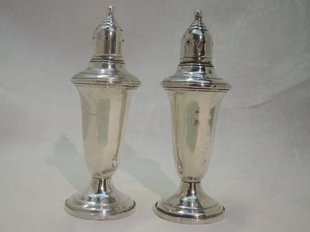 A pair of white metal oversized pepperettes stamped Empire sterling of urn form having clear glass