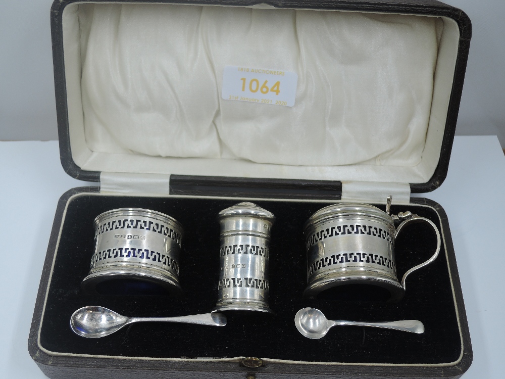 A cased silver three piece condiment set of drum form having pierced decoration and blue glass