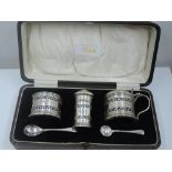 A cased silver three piece condiment set of drum form having pierced decoration and blue glass