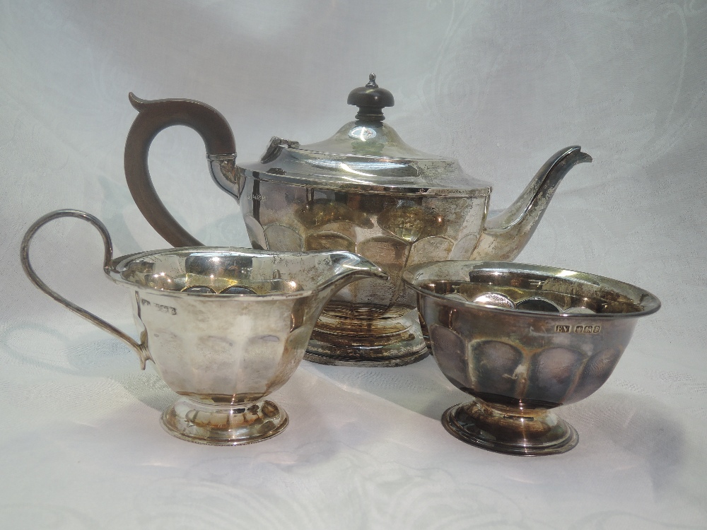 A silver three piece matched tea set of circular form having facetted decoration, fruitwood handle