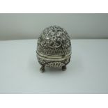 A white metal pounce pot of egg form having trefoil scallop and bun feet, repousse floral and scroll