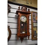 A wooden cased chiming wall clock having carved details and finials to top.