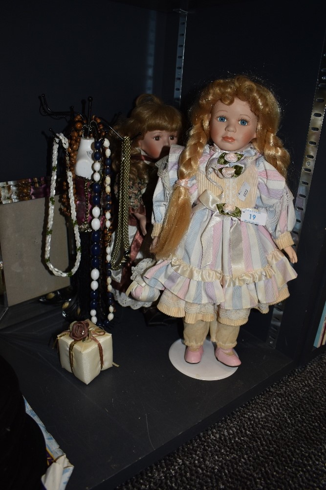 Two dolls with stands, a selection of necklaces and a mirrored photo frame.