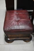 A hard wood foot stool storage case with wine red leather top