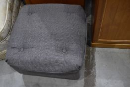 A grey upholstered footstool on casters