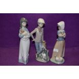 Three Lladro Nao figurines, two girls with puppies and a boy with dog at his feet.
