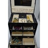 A black travel jewellery box containing a selection of costume jewellery including wrist watches,