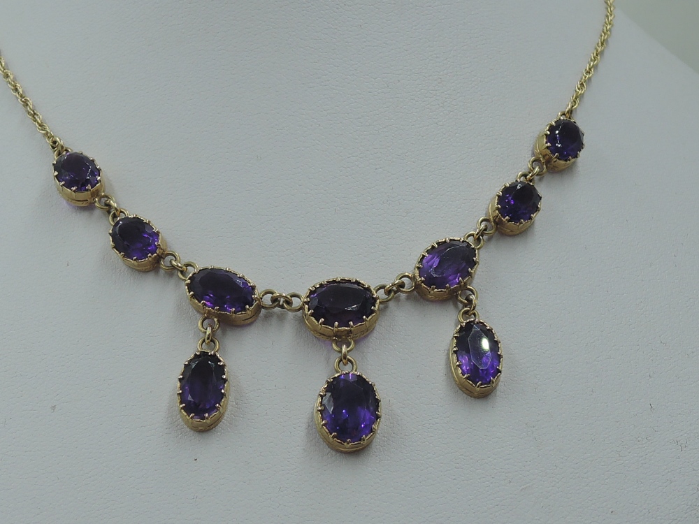 A ten stone heat treated amethyst necklace having seven graduated stones with three drops on a fixed