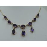 A ten stone heat treated amethyst necklace having seven graduated stones with three drops on a fixed