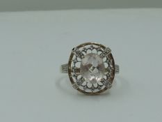 A lady's dress ring having a morganite style oval stone within an open border having diamond chip