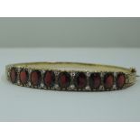 A 9ct gold hinged bangle set with nine oval garnets interspersed by pairs of diamond chips in a
