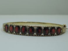 A 9ct gold hinged bangle set with nine oval garnets interspersed by pairs of diamond chips in a