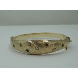 A 9ct gold hinged bangle having diamond and emerald chip decoration in star burst settings on