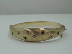 A 9ct gold hinged bangle having diamond and emerald chip decoration in star burst settings on