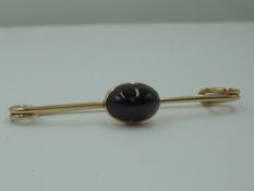 A yellow metal bar brooch in the form of a safety pin having a garnet cabouchon, no marks tests as