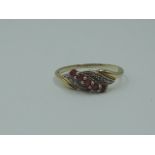 A lady's dress ring having a row of ruby style stones in a swirl illusionary mount on yellow metal