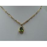 A peridot tear drop shaped pendant having diamond chip decoration in a yellow metal mount stamped 9K