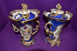 A pair of continental mantle urns in porcelain hand painted with floral scenes on blue grounds