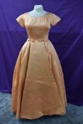 A vintage late 1950s/early 1960s apricot satin gown having bows to pleated waist and train detail to