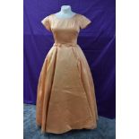 A vintage late 1950s/early 1960s apricot satin gown having bows to pleated waist and train detail to