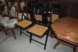 A set of four ebonised folding chairs, having cane seats