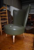 A vintage low seat nursing chair having green leatherette upholstery on tapered round legs with