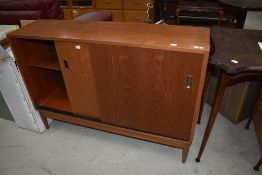A vintage teak or sapele style office low bookcase having sliding ply doors, on tapered legs,