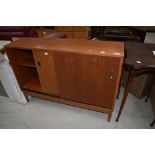 A vintage teak or sapele style office low bookcase having sliding ply doors, on tapered legs,