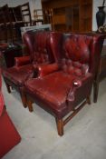 A pair of traditional burgundy leather button back wing armchairs