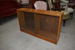 A vintage golden oak low bookcase, having sliding glass doors, dimensions approx. W107 D22 H63cm