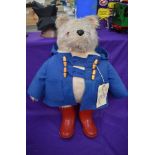 A Gabrielle Designs plush covered Padding Bear soft toy, wearing blue jacket and red wellingtons,