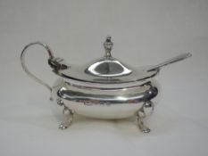 An early 20th Century silver mustard pot of boat form having quatrefoil paw feet, hinged lid and