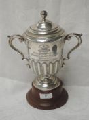 An Edwardian silver lidded trophy with wooden stand having gadrooned decoration, moulded loop