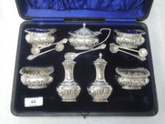 A cased silver seven piece condiment set having repousse decoration and blue glass liners, Chester