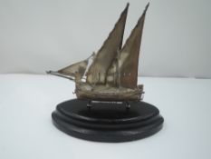 A small HM silver model of a sailing boat stamped 925 on a wooden plinth