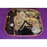 A vintage tin containing a selection of broken strings of beads and simulated pearls etc