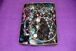 A tin of costume jewellery necklaces of various forms