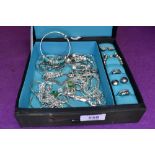 A material jewellery box containing a selection of white metal costume jewellery including