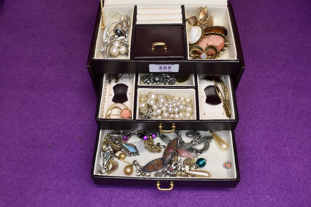 A small maroon travel jewellery box containing a selection of costume jewellery including cameo