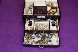 A small maroon travel jewellery box containing a selection of costume jewellery including cameo