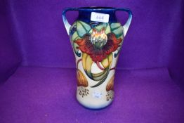 A large Moorcroft twin handled lily vase having cream and blue ground with lily pattern in ochre,