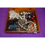 A small wooden display box containing a selection of costume jewellery necklaces, including