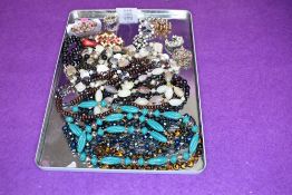 Nine strings of beads of various forms and a small selection of costume brooches including ceramic