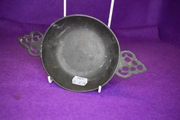 A traditional pewter porringer bowl with pierced handles