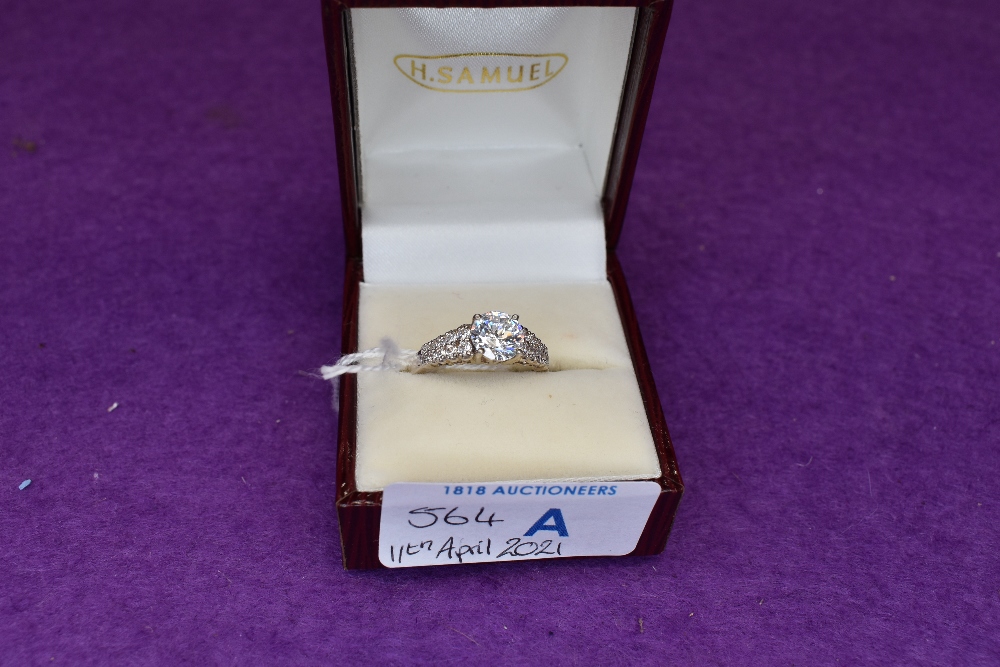 A lady's dress ring having a cubic zirconia solitaire to CZ set shoulders on a white metal loop