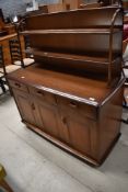 A dark stained Ercol sideboard having plate rack to back, bifold door and Shepherd castors