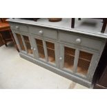 A grey painted sideboard having three frieze drawers over triple cupboard, having mesh panel fronts,